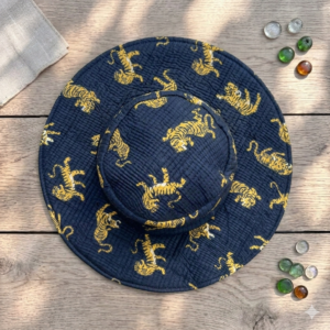 Top-down-view-of-a-navy-blue-quilted-wide-brim-sun-hat-decorated-with-a-repeating-pattern-of-golden-yellow-tigers-resting-on-a-wooden-surface-next-to-glass-pebbles