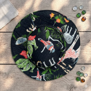 Top-down-view-of-a-black-quilted-wide-brim-sun-hat-decorated-with-a rich-jungle-pattern-featuring illustrated-safari-animals-like-zebras-and-giraffes-with tropical-foliage-placed-on-a-wooden-surface