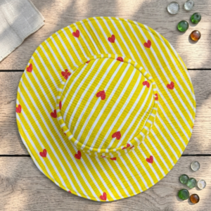 Overhead-view-of-a-yellow-and-white-striped-quilted-wide-brim-bucket-hat-decorated-with-a-repeating-pattern-of-small red-hearts-placed-on-a-dark-surface.