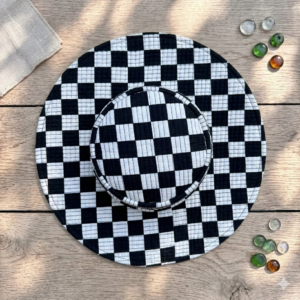 Quilted-wide-brim-bucket-hat with-a-black-and-white-checkerboard-pattern-displayed-from-a-top-down-angle-on-a-dark-fabric-background.