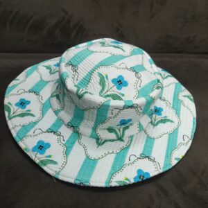 A-white-and-mint-green-vertically-striped-quilted-wide-brim-bucket-hat featuring-vintage-inspired-framed-blue-flowers-with-green-leaves-shown-on-a-dark-fabric-background.