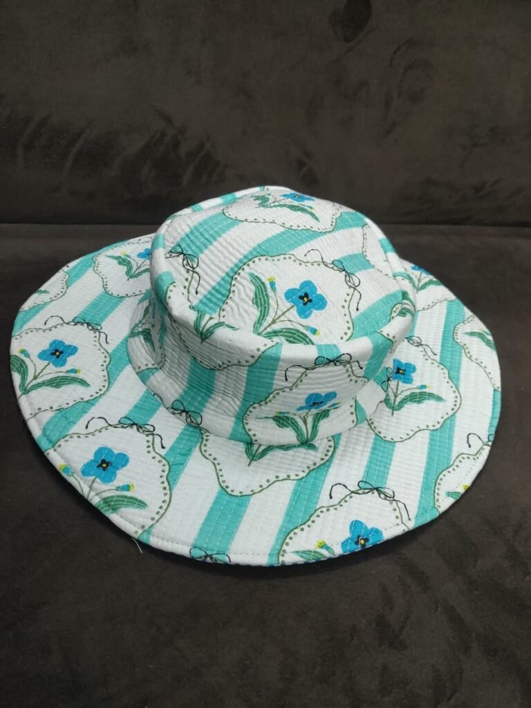 A-white-and-mint-green-vertically-striped-quilted-wide-brim-bucket-hat featuring-vintage-inspired-framed-blue-flowers-with-green-leaves-shown-on-a-dark-fabric-background.