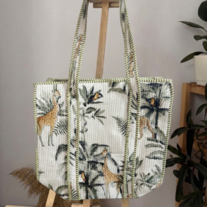 Front-view-photo-of-a-white-quilted-tote-bag-with-a green-jungle safari-print-of-giraffes-and birds-hanging-on-a-wooden-stand